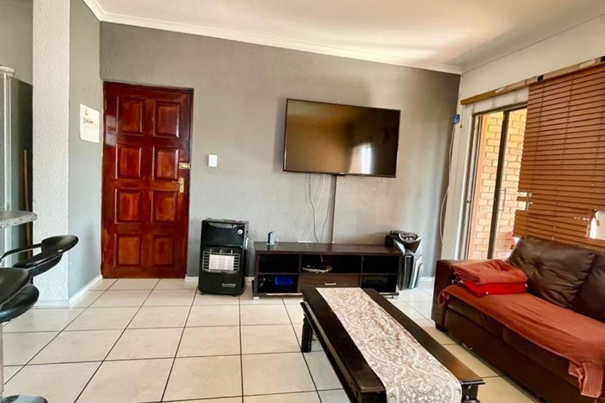 A living room featuring tiled flooring, a wooden door, and a sliding glass door with venetian blinds, providing access to the exterior.