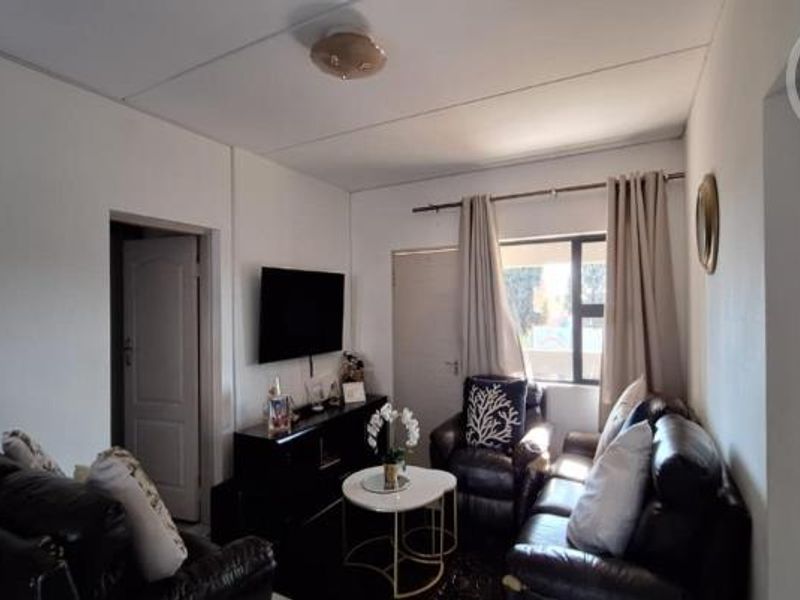 A compact living room featuring neutral walls, a ceiling light fixture, and access to adjacent rooms via internal doors.