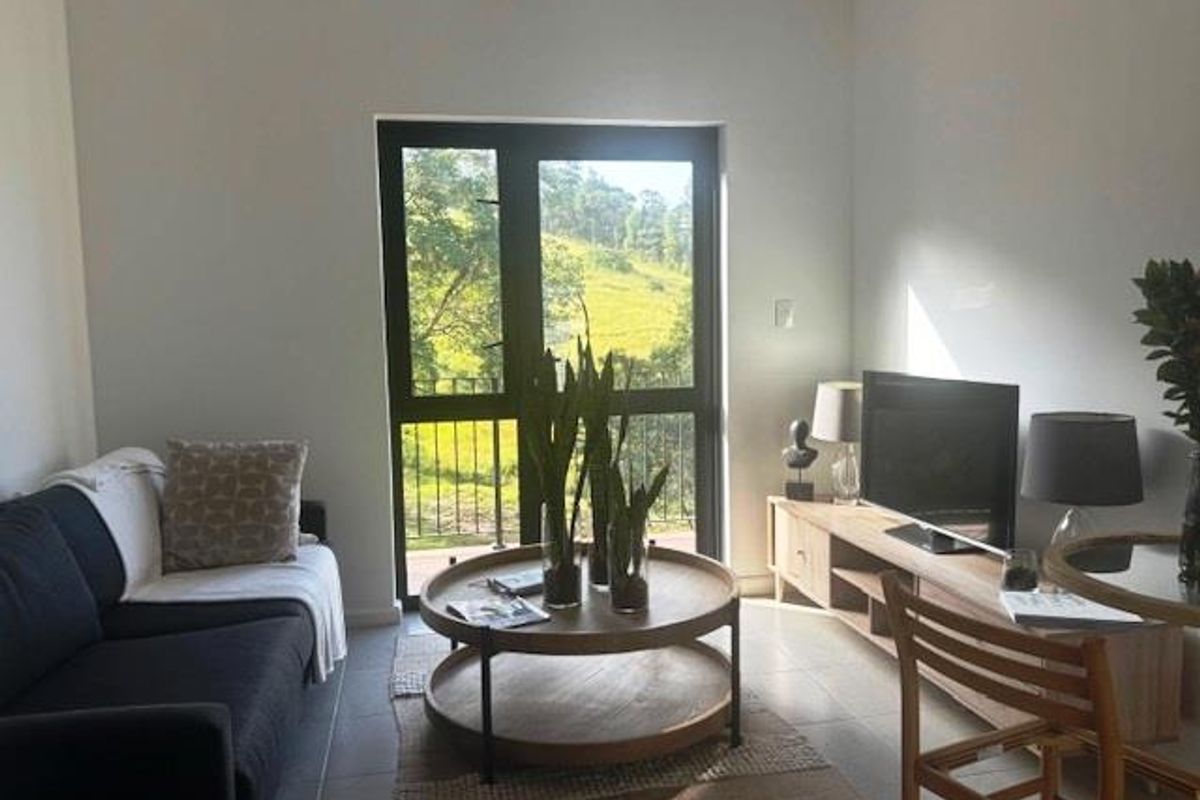 A bright living room featuring tiled flooring and a glass door leading to an outdoor balcony with scenic views.