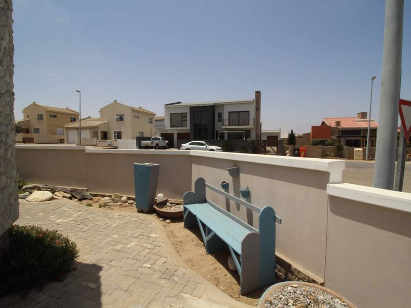 A view of the front boundary wall and paved walkway leading to the property entrance, featuring stone cladding and a clean exterior finish.