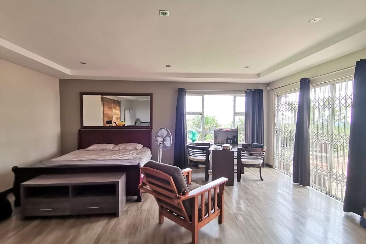 Spacious bedroom featuring recessed ceiling lighting, wood-look flooring, and large sliding glass doors with security gates leading to an outdoor area.