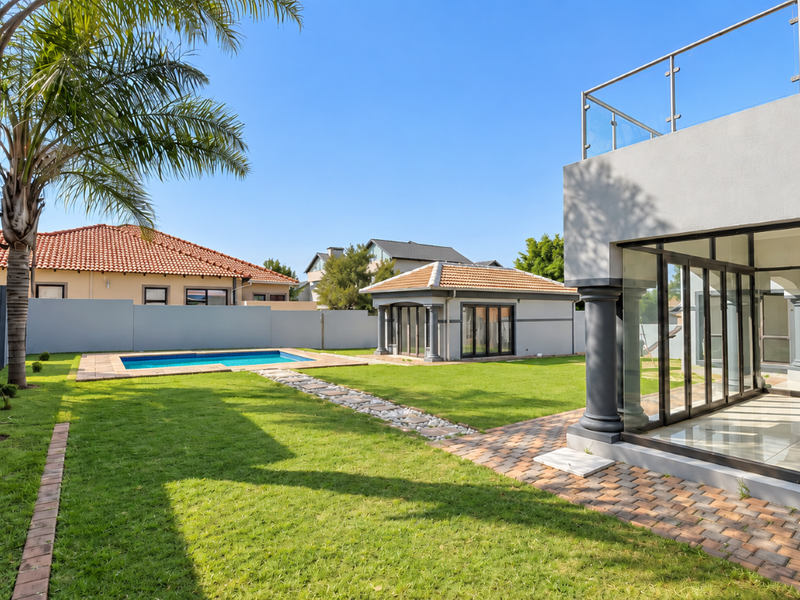 A well-maintained rear garden featuring a swimming pool, manicured lawn, paved pathways, and a modern detached outbuilding with glass sliding doors.