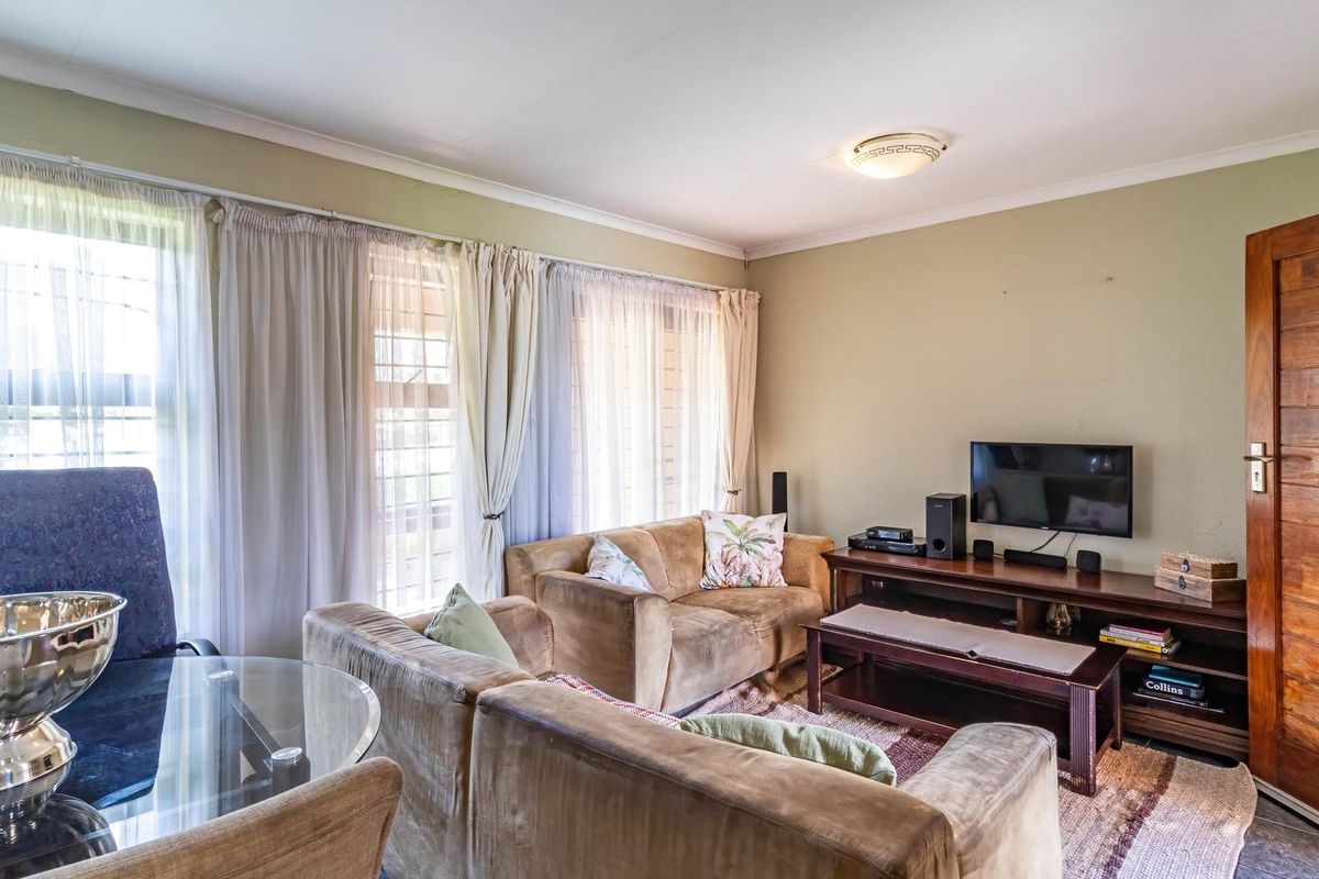 A comfortable living room featuring a solid wood entrance door, large windows with security bars, and neutral wall finishes.