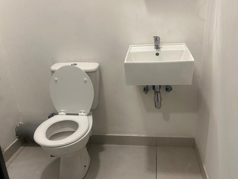 A compact bathroom featuring a wall-mounted basin, toilet, and tiled flooring, currently presenting in a basic, functional condition.