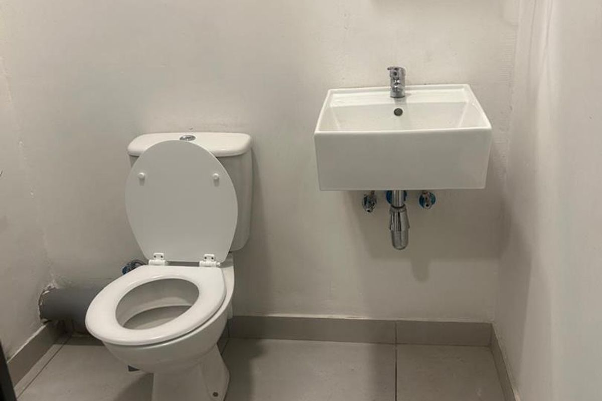 A compact bathroom featuring a wall-mounted basin, toilet, and tiled flooring, currently presenting in a basic, functional condition.