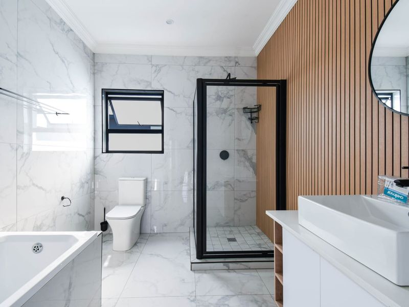 Modern bathroom featuring marble-look tiling, a slatted wood accent wall, a walk-in shower with black fixtures, a bathtub, and a sleek vanity.