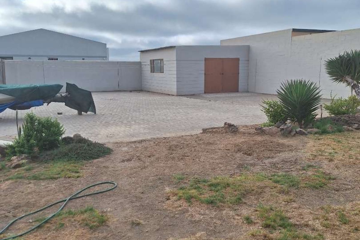 A spacious rear yard featuring a paved area, a detached outbuilding with double doors, and an expansive, partially landscaped garden space.