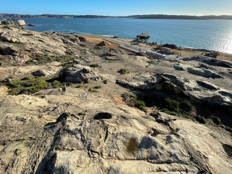 An elevated view of the rocky coastal landscape overlooking the ocean and nearby waterfront infrastructure.