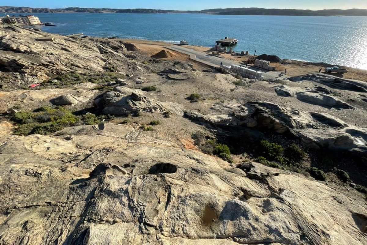 An elevated view of the rocky coastal landscape overlooking the ocean and nearby waterfront infrastructure.