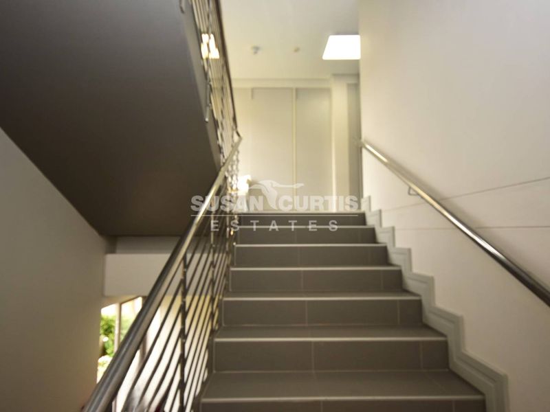 A clean, modern staircase featuring tiled steps, a stainless steel balustrade, and built-in storage cupboards at the landing.