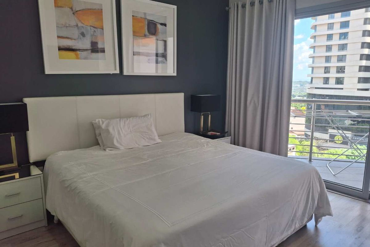 A well-maintained bedroom featuring laminate flooring and a sliding glass door that opens onto a balcony with urban views.