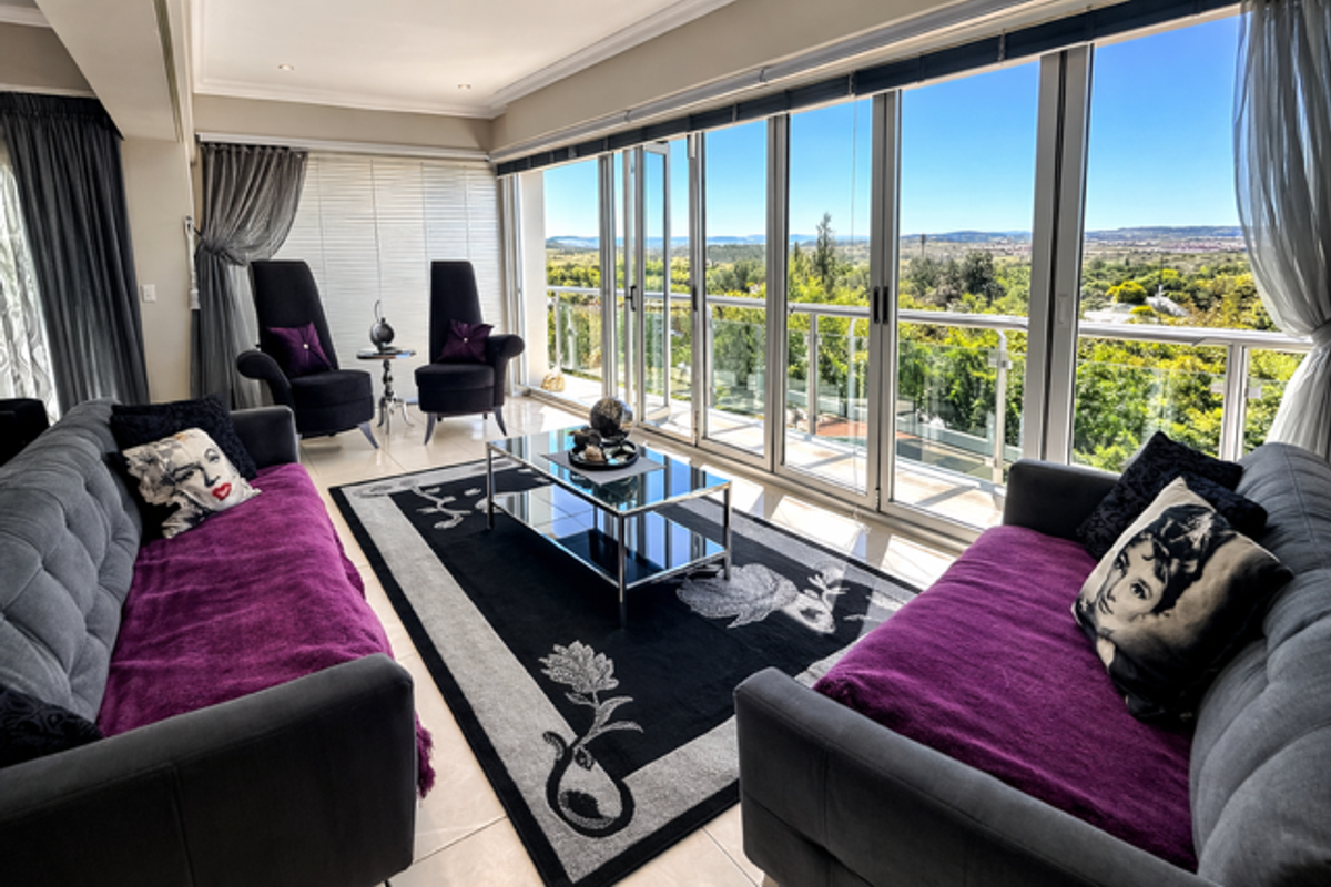 A bright living room featuring large floor-to-ceiling glass sliding doors that open onto a balcony with expansive scenic views.