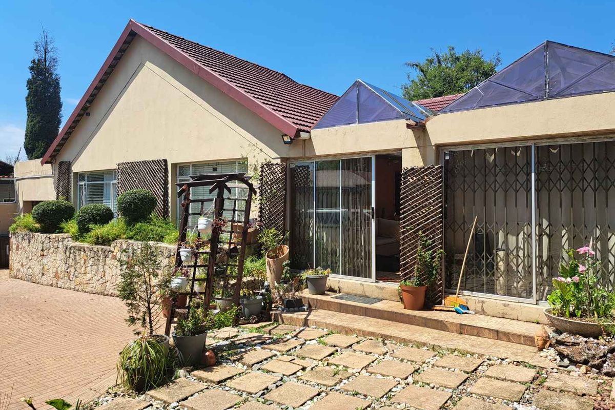 Rear exterior view featuring a paved patio area, stone retaining wall, sliding glass doors, and integrated skylights under a tiled roof.
