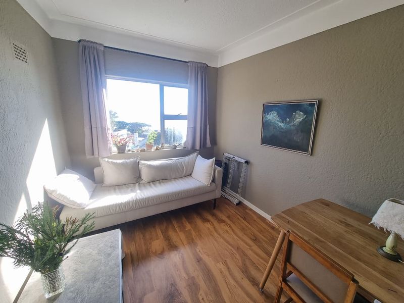 A bright living room featuring laminate flooring, coved ceilings, and a large window providing natural light and an exterior view.
