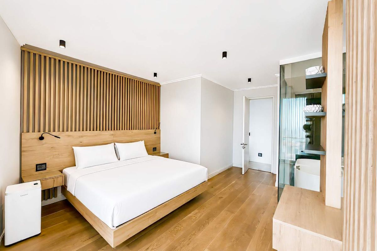 Modern bedroom featuring timber slat wall paneling, integrated bedside lighting, hardwood flooring, and an en-suite bathroom with glass partition.
