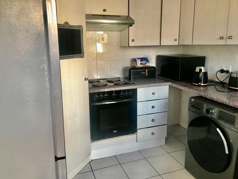 Functional kitchen featuring built-in cabinetry, electric oven with hob, extractor fan, and tiled flooring, offering a practical layout for daily meal preparation.