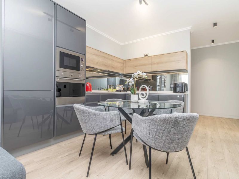 Modern open-plan kitchen featuring high-gloss cabinetry, integrated appliances, a mirrored splashback, and light wood-look laminate flooring in a well-lit, contemporary space.