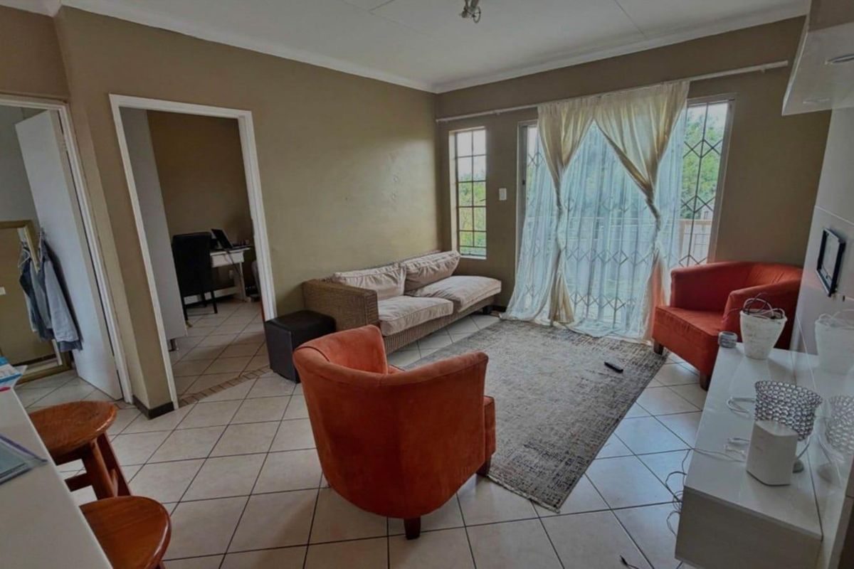 A living room featuring tiled flooring, large windows with security gates, and direct access to an outdoor area, providing a functional and connected living space.