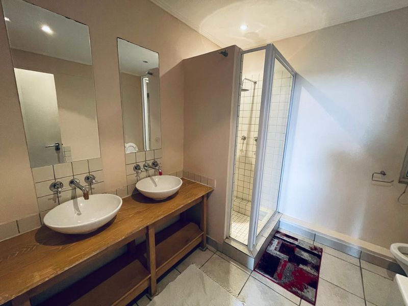 Bathroom featuring a double vanity with vessel sinks, wall-mounted faucets, and a separate glass-enclosed shower with tiled finishes.