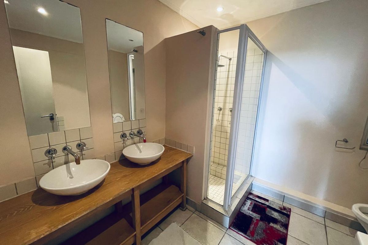 Bathroom featuring a double vanity with vessel sinks, wall-mounted faucets, and a separate glass-enclosed shower with tiled finishes.