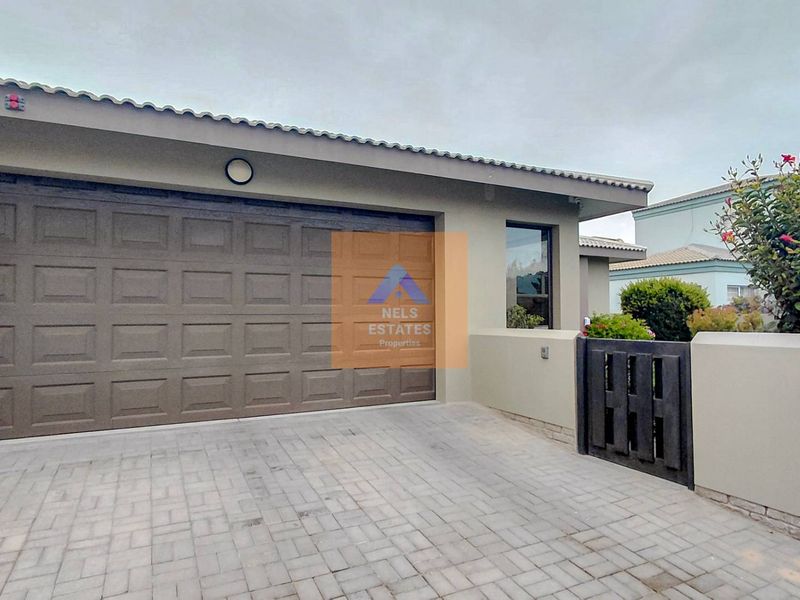 Front elevation of the property featuring a paved driveway, a sectional garage door, and a secure pedestrian gate with boundary walling.