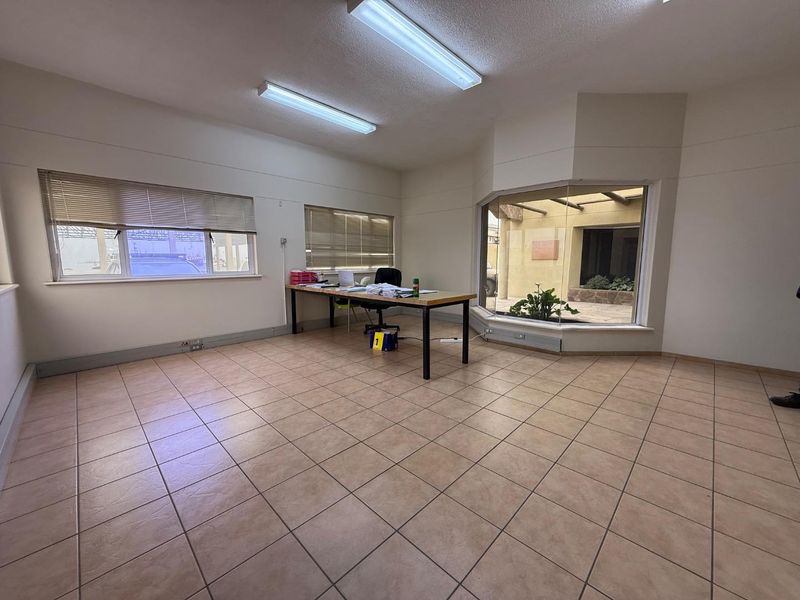 Spacious office area featuring ceramic tile flooring, large bay window, and functional fluorescent lighting, suitable for a professional workspace.