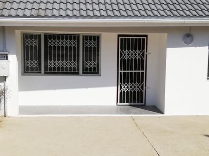Front elevation of a cottage featuring a tiled roof, security gate, and security bars on the windows, with an unfinished concrete driveway area.