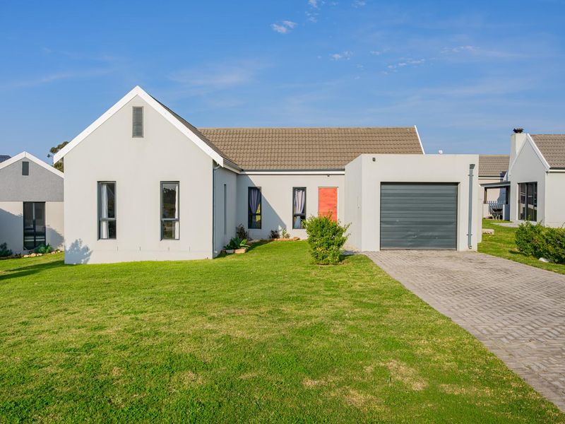 A well-maintained single-story residential house featuring a paved driveway, integrated garage, and a neat front lawn under a clear blue sky.