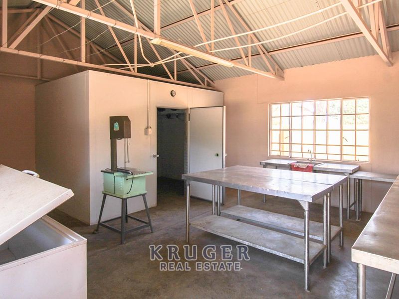 A functional utility or processing space featuring stainless steel prep tables, an integrated walk-in cold storage unit, and exposed roof trusses.