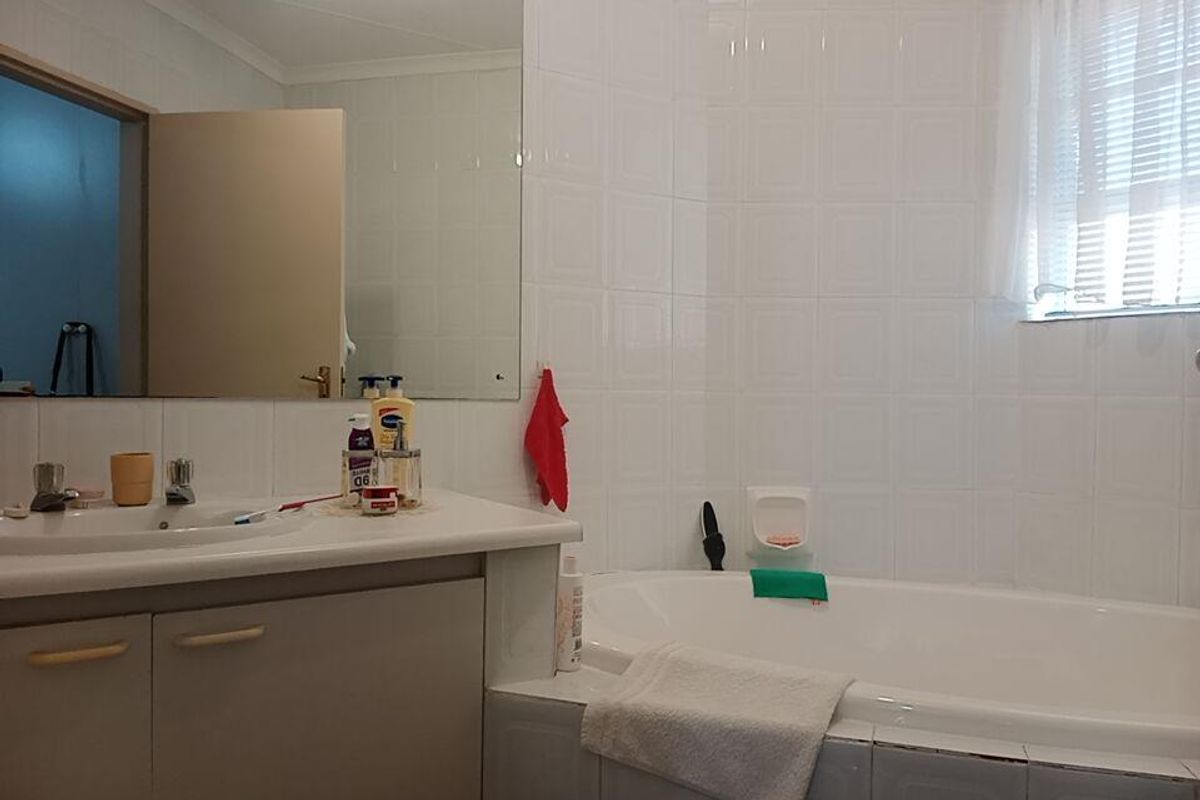 A functional bathroom featuring a built-in bathtub, vanity basin with storage cabinetry, and wall-to-wall tiling.