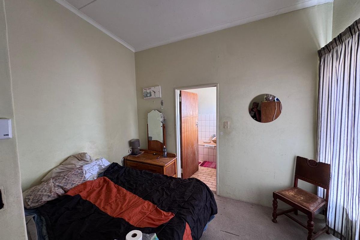 A bedroom featuring carpeted flooring and an en-suite bathroom access, requiring cosmetic updates to improve the overall finish.