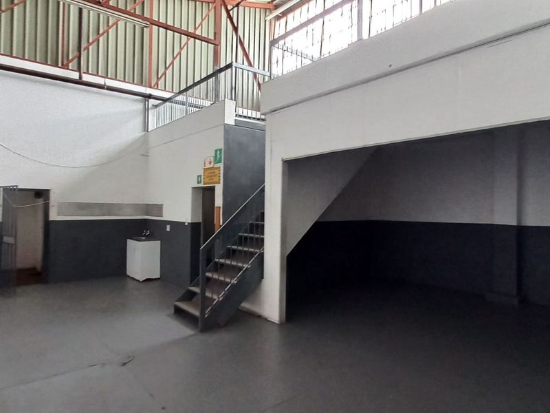 Spacious industrial utility area featuring a mezzanine level, metal staircase, and high ceilings with exposed steel trusses, suitable for storage or workshop use.