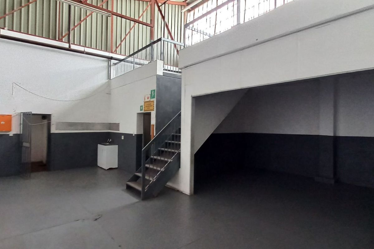 Spacious industrial utility area featuring a mezzanine level, metal staircase, and high ceilings with exposed steel trusses, suitable for storage or workshop use.