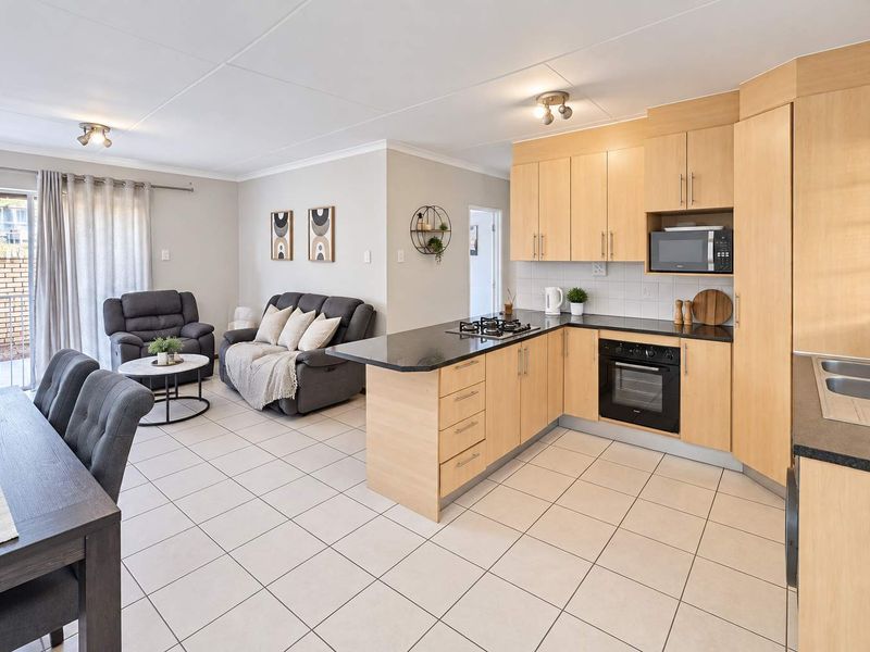 Open-plan living and kitchen area featuring light wood cabinetry, gas hob, built-in oven, and tiled flooring with direct access to a patio.