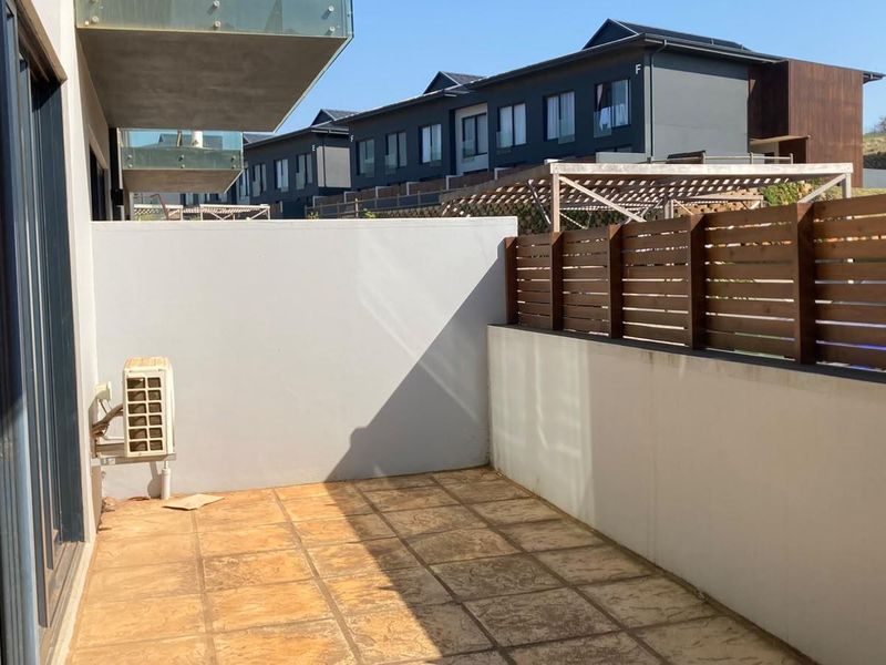 A private ground-floor patio featuring tiled flooring, a timber privacy screen, and a masonry boundary wall, providing a functional outdoor space.