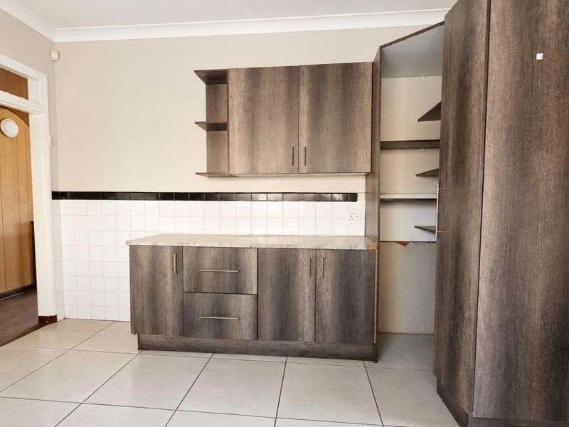 A kitchen area featuring dark wood-look cabinetry, tiled splashback, and tiled flooring, currently requiring minor repairs to cabinetry and wall finishes.