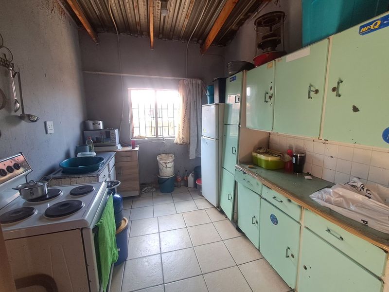 A functional kitchen space featuring original cabinetry, tiled flooring, and exposed ceiling rafters, offering significant potential for modernization and renovation.