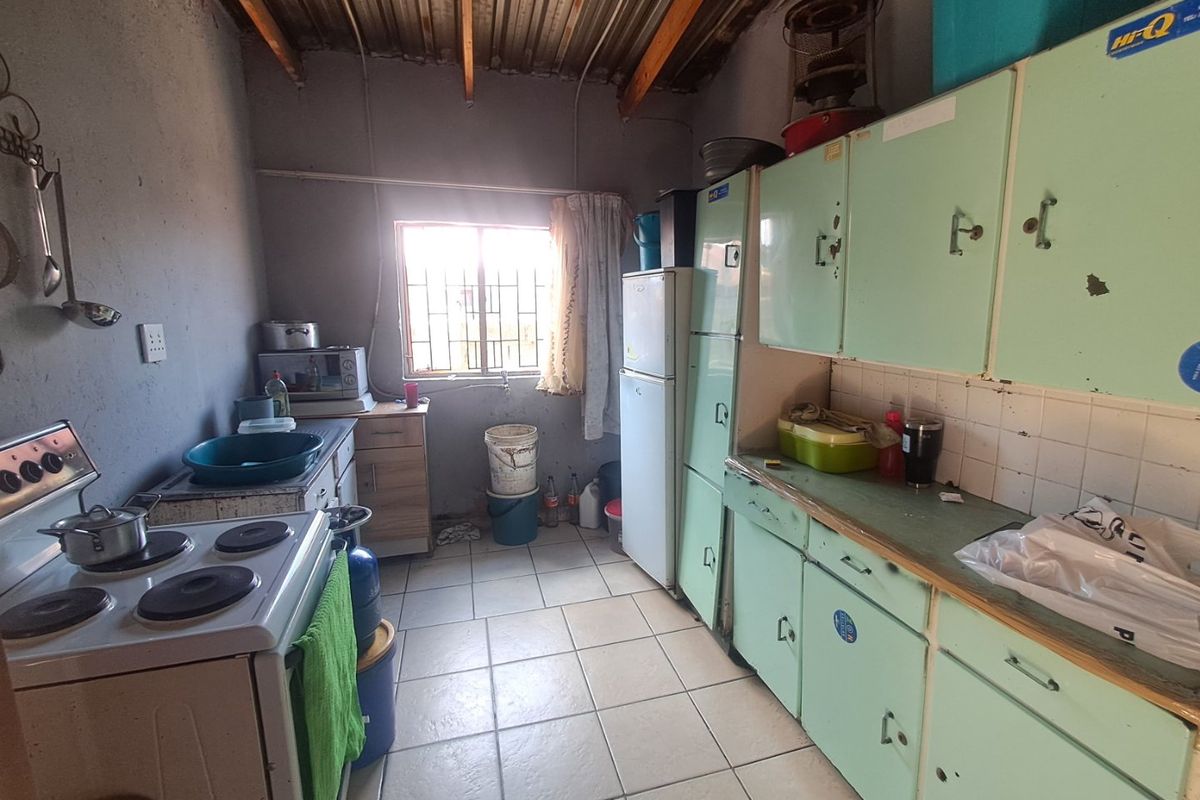 A functional kitchen space featuring original cabinetry, tiled flooring, and exposed ceiling rafters, offering significant potential for modernization and renovation.