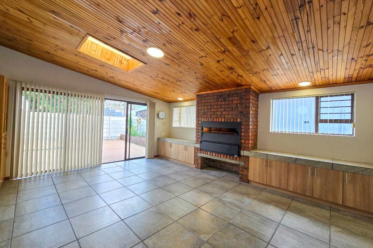 Spacious living area featuring a prominent brick fireplace, built-in cabinetry, tiled flooring, and a vaulted timber-clad ceiling with a skylight.