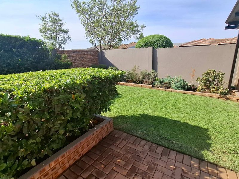 A well-maintained private garden featuring a manicured lawn, brick-paved patio area, and established perimeter walling with neat hedging.