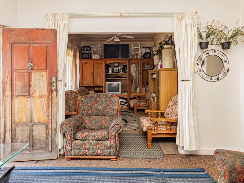 A living room area featuring an arched entryway, a ceiling fan, and a weathered timber door leading to an outdoor space.