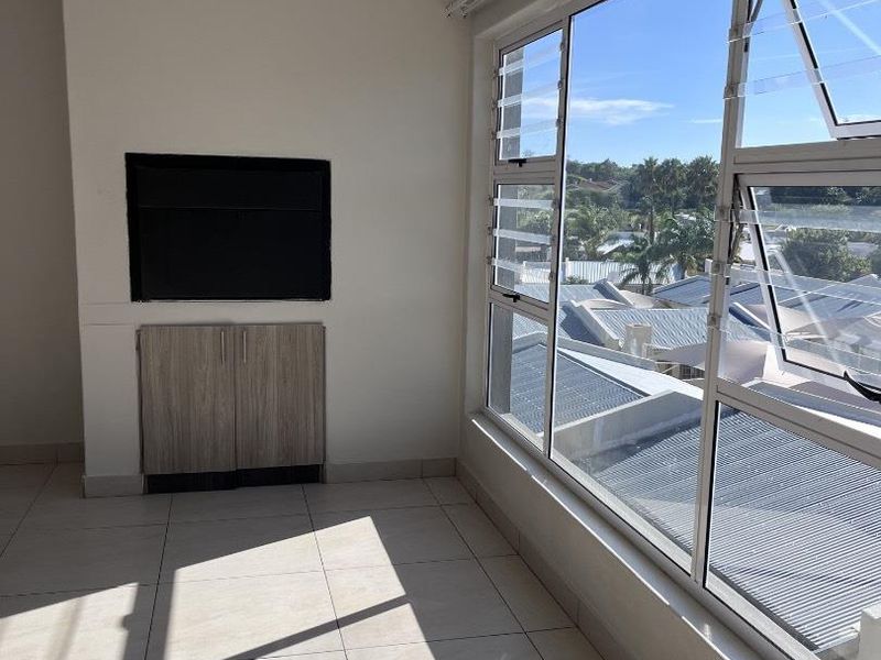 Bright and spacious living area featuring large windows with neighbourhood views, tiled flooring, and built-in cabinetry.