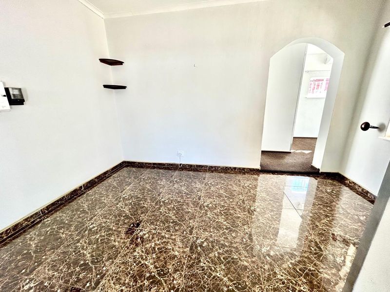An empty living area featuring polished marble-look floor tiles and a classic arched doorway leading to an adjacent space.