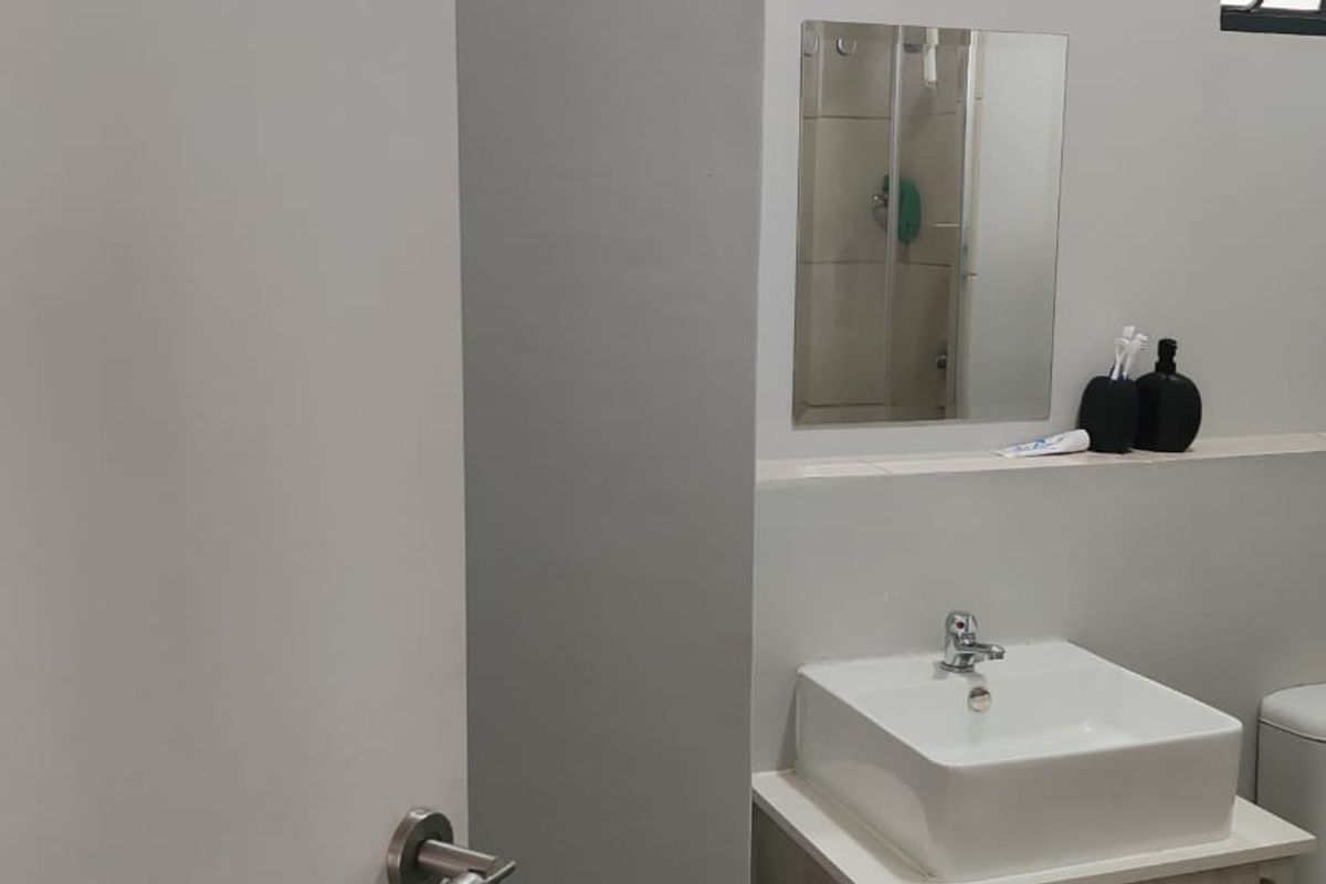 A modern bathroom featuring a square vessel sink, wall-mounted mirror, and a glass-enclosed shower area with neutral tiling.