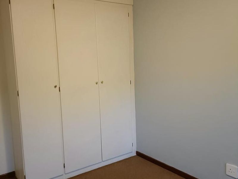A clean, empty bedroom featuring neutral wall paint, carpeted flooring, and functional built-in cupboards with white doors.