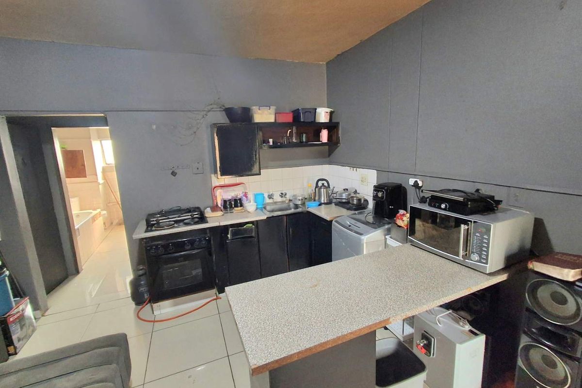Compact kitchen featuring built-in cabinetry, a gas stove with oven, and a breakfast counter, with a view into the adjacent bathroom.