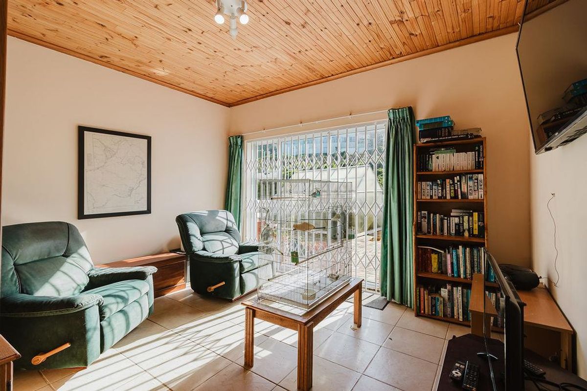 A living room featuring a timber-clad ceiling, tiled flooring, and a sliding glass door with a security gate leading to the exterior.