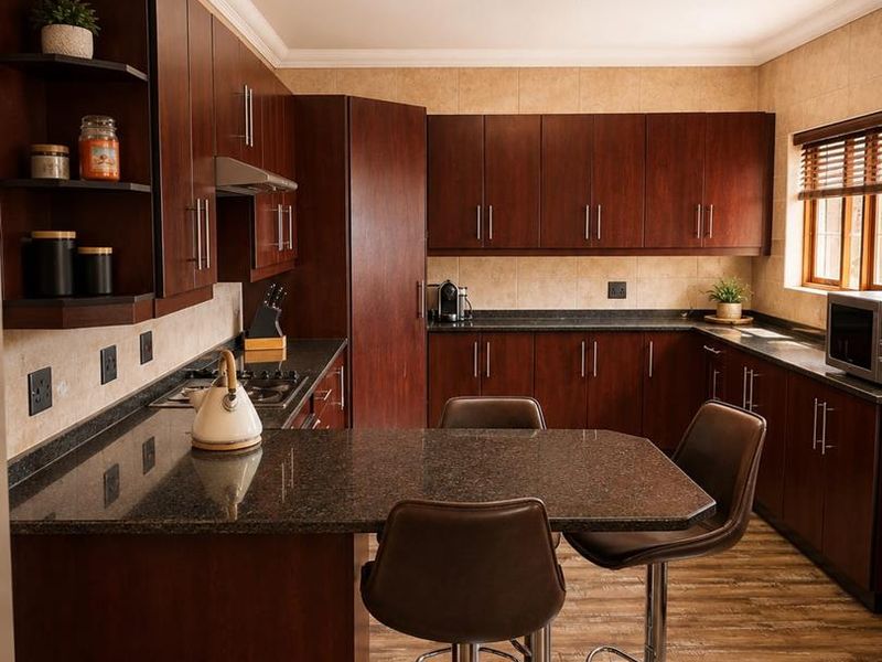 A well-maintained kitchen featuring dark wood cabinetry, granite countertops, a built-in gas hob, and a breakfast bar area with laminate flooring.