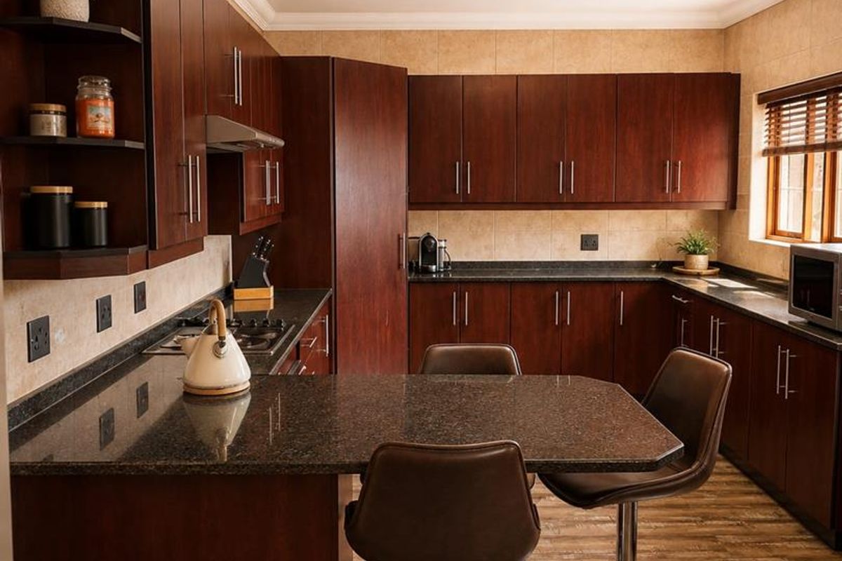 A well-maintained kitchen featuring dark wood cabinetry, granite countertops, a built-in gas hob, and a breakfast bar area with laminate flooring.