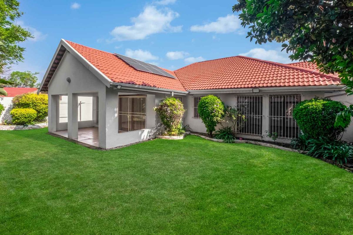 Rear view of the property featuring a tiled roof with solar panels, a covered patio area, and a well-maintained lawn and garden.
